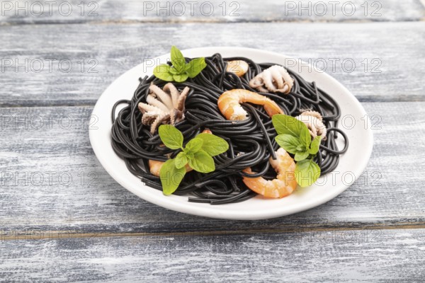 Black cuttlefish ink pasta with shrimps or prawns and small octopuses on gray wooden background. Side view, close up