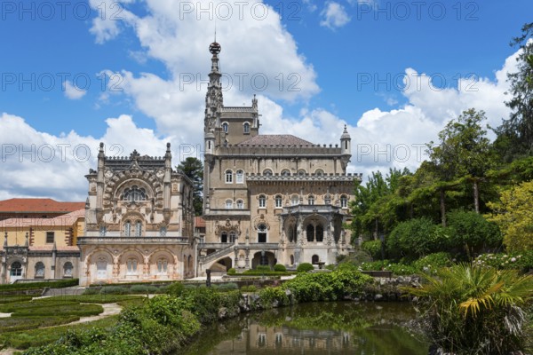 Ein prächtiges Schloss mit aufwendiger Architektur und Türmen vor einem blauen Himmel mit Wolken, umgeben von einem gepflegten Garten mit Teichen, Palácio Hotel do Buçaco, Mata Nacional do Buçaco, National-Wald von Bussaco, Bucaco, Mealhada, Beira Litoral, Portugal, Europe