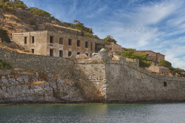 Dilapidated-looking old buildings on a rocky coastline surrounded by clear skies and calm seas, Venetian Sea Fortress, Leper Island, Spinalonga, Elounda Bay, Mirabello Bay, East Crete, Crete, Greek Islands, Greece, Europe