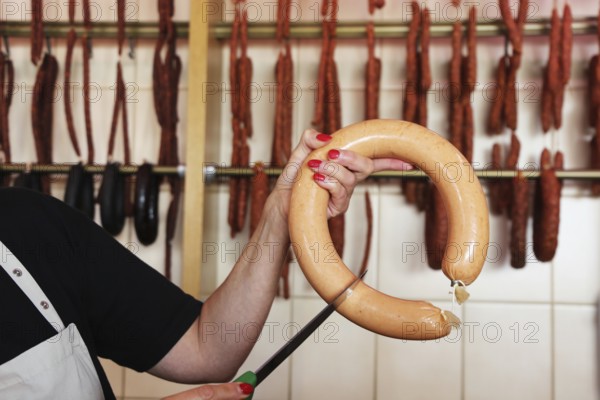 Saleswoman in the butcher's shop holds a knife to a sausage