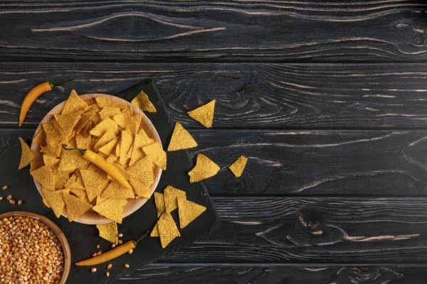 Bowl of tortilla chips next to raw sweetcorn and yellow peppers on a dark wooden table