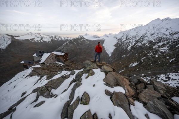 Mountaineer looking at mountain panorama and glacier, mountain hut Ramolhaus in autumn with snow, at sunset, view of Gurgler Ferner with summit Hochwilde and Falschungsspitze, Ötztal Alps, Tyrol, Austria, Europe