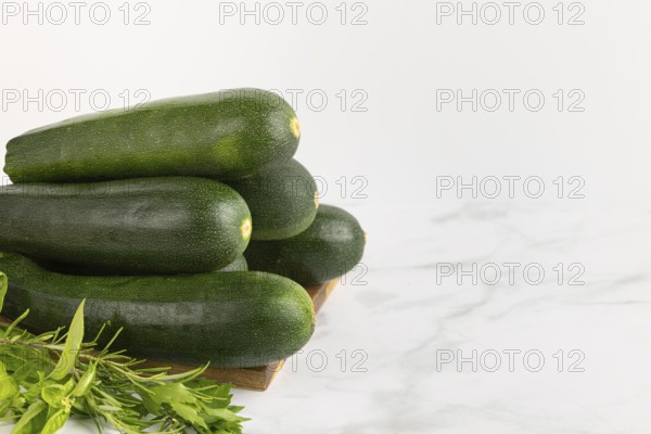 Fresh courgettes stacked on a wooden board with fresh herbs against a light-coloured background