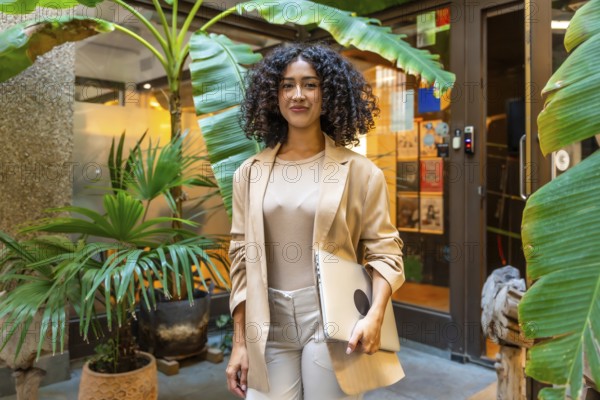 Three quarter length portrait of a beauty young businesswoman standing carrying a laptop next to coworking office
