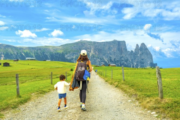 Mother and son enjoying a summer hike in the picturesque landscape of alpe di siusi, with the majestic sciliar mountain in the background