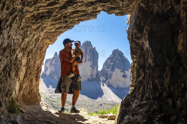 Father holding son admiring tre cime di lavaredo from inside a Tre Cime Cave during a trekking tour in the dolomites
