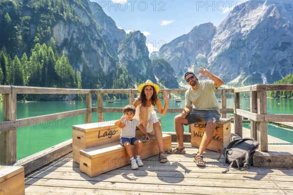 Happy family waving at lake braies, also known as pragser wildsee, enjoying summer vacation amidst the stunning scenery of the dolomites in italy