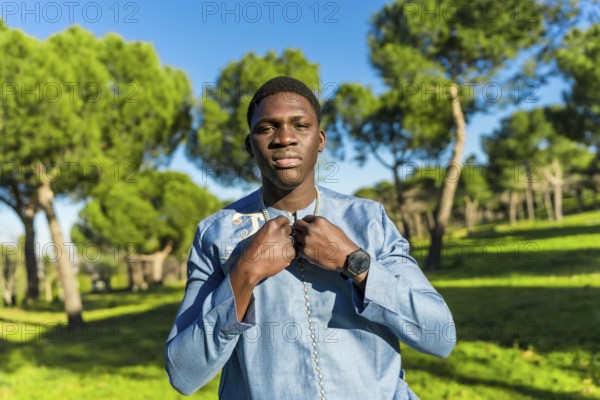 Young senegalese man wearing traditional dashiki attire, posing in a serene park setting, showcasing cultural pride and timeless fashion