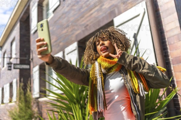 Low angle view of a cheerful latin young woman with curly hair taking selfie outside a residential house