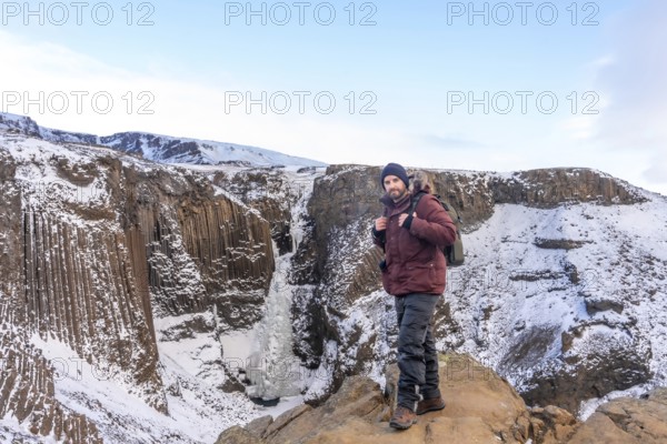 Portrait of a hiker at frozen Hengifoss waterfall in cold Iceland winter, volcanic cliffs