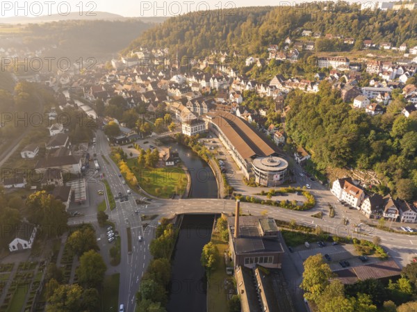 Aerial view of a town with a river surrounded by hills and green vegetation at sunset, centred on a main street and buildings, Calw, Black Forest, Germany, Europe