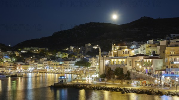 Illuminated coastal town at night with moon in the sky and water in the foreground, Rising full moon, Pigadia, town and harbour, Pigadia Bay, main town, Karpathos, Dodecanese, Greek Islands, Greece, Europe