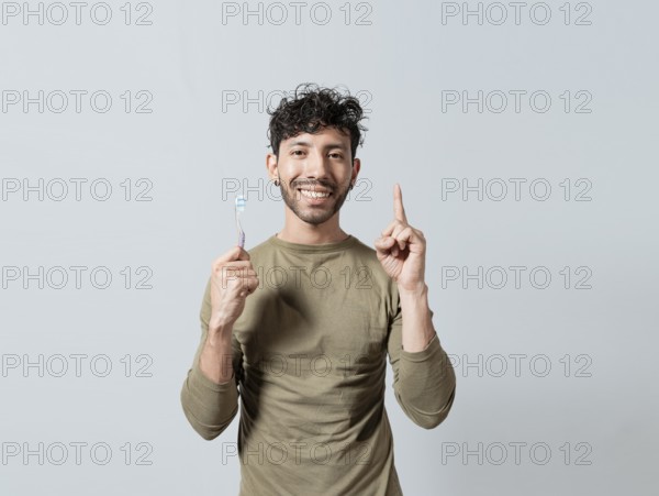 Smiling young man holding dental brush pointing up. Handsome guy holding toothbrush pointing an advertisement up