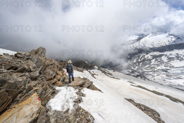 Mountaineer on a rocky ridge with snow, descent from the summit of Schönbichler Horn, view of snow-covered mountain peaks and valley Zemmgrund, Berliner Höhenweg, Zillertal Alps, Tyrol, Austria, Europe