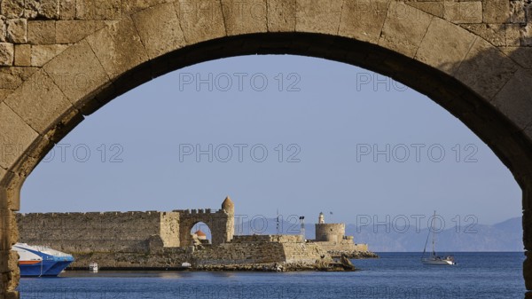 View through a stone window arch to the sea and a small castle in the background, De Naillac Tower, Fort of Saint Nikolaos, harbour area, Rhodes Town, Rhodes, Dodecanese, Greek Islands, Greece, Europe