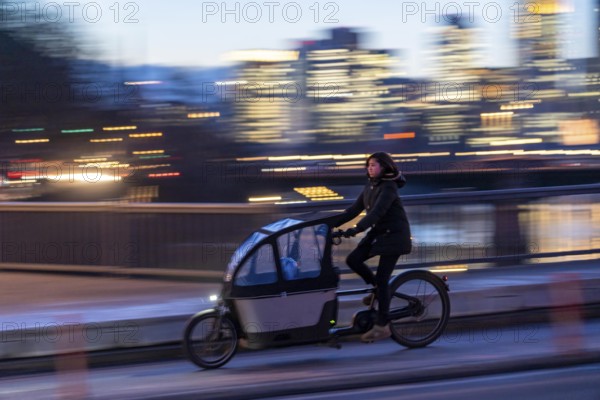 Skyline of the city centre of Frankfurt am Main, cargo bike cyclist on the rafter bridge, dusk, river Main, winter, Hesse, Germany, Europe