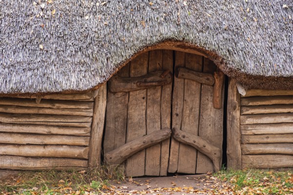 Entrance to a longhouse built of tree logs and a detached roof of reeds