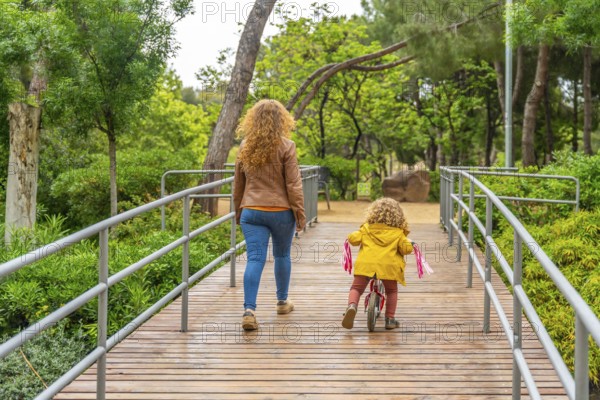 Rear view of a caucasian mother and little girl walking and cycling on a park