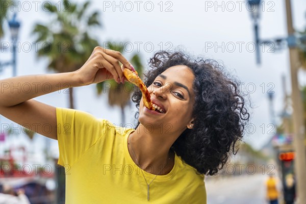 Latin woman with curly hair enjoying take away pizza in the street