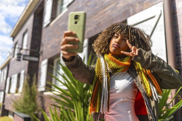 Beauty latin woman gesturing victory while taking a selfie standing next to a house