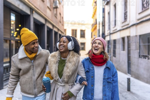Three cheerful multi ethnic young friends walking arm in arm in the city on a winter day, enjoying their time together