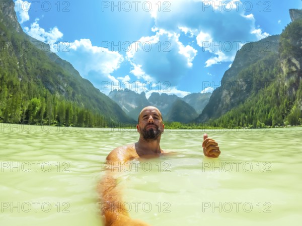 Tourist gesturing thumbs up while swimming in the turquoise water of lago di landro, surrounded by the breathtaking dolomites landscape on a sunny summer day