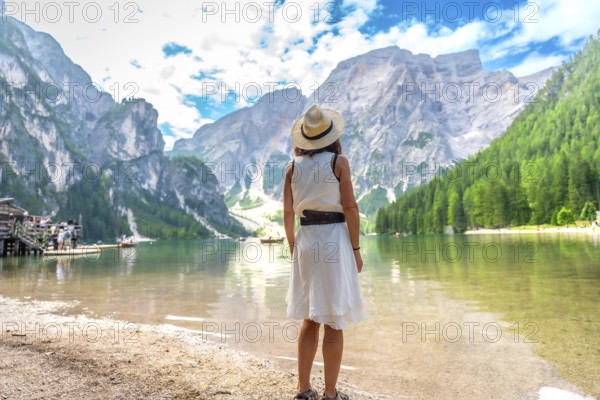 Woman admiring the stunning landscape of lake braies, surrounded by majestic mountains and lush greenery, during a summer day in the italian dolomites