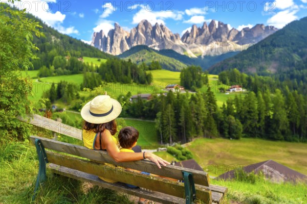 Mother and son enjoying a relaxing moment on a bench, admiring the breathtaking panorama of the odle mountains in val di funes, dolomites, italy