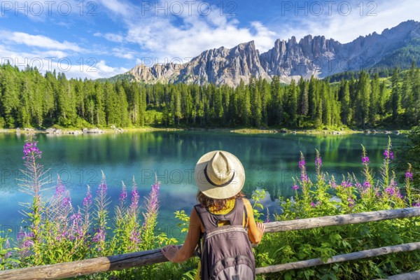 Female tourist admiring the stunning turquoise waters of lake carezza with the latemar mountain range in the background, dolomites, italy