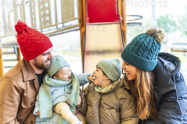 Happy family wearing winter clothes is having fun at the playground, enjoying precious moments together