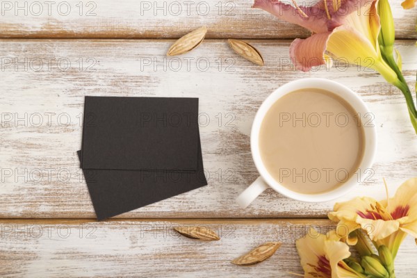 Black paper business card mockup with orange day-lily flower and cup of coffee on white wooden background. Blank, top view, flat lay, copy space, still life. spring concept