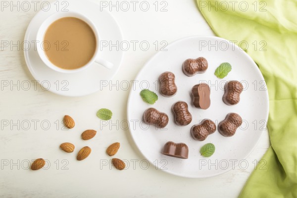 Chocolate candies with almonds and a cup of coffee on a white wooden background and green textile. top view, flat lay, close up