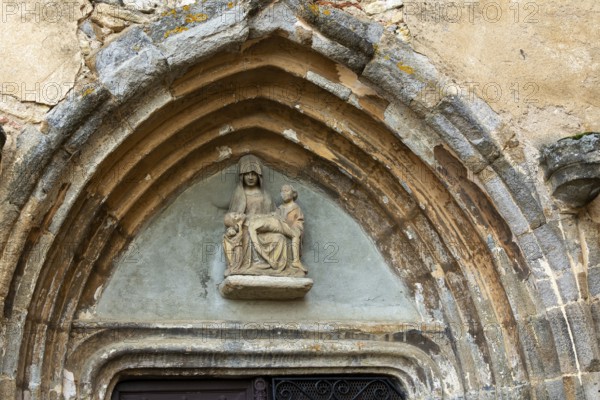 Sculpture of Pieta is prominently displayed above the portal of the church in Collanges, Puy de Dome. Auvergne-Rhone-Alpes. France