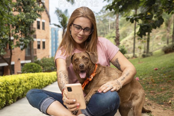 Woman sitting with reading glasses taking a selfie with her pet sitting in the park