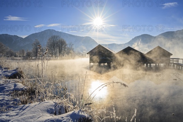 Boat huts in the morning light in front of mountains, lake, snow, winter, sunbeams, fog, Lake Kochel, foothills of the Alps, Bavaria, Germany, Europe