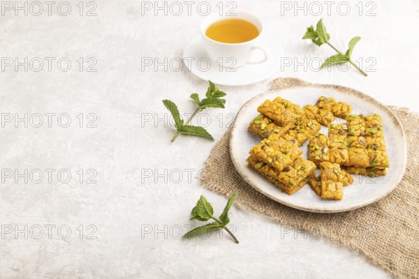 Traditional iranian dessert sohan with cup of green tea on a gray concrete background and linen textile. side view, copy space