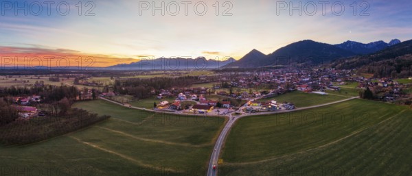 Panoramic view of a village in a wide green plain with mountains in the background at dusk, Bad Feilnbach