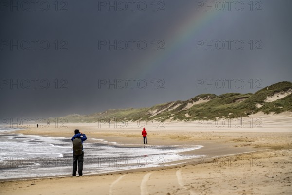 Walkers on the beach, dark storm clouds, choppy sea, autumn on the North Sea in North Holland, between the towns of Egmond aan Zee and Bergen aan Zee, Netherlands