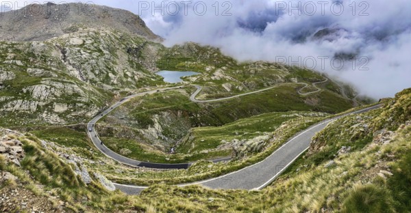 In the foreground a winding pass road to the Colle del Col de Nivolet pass, in the background a small lake naturally dammed by snowmelt, Gran Paradiso National Park, Ceresole Reale, Piedmont, Italy, Europe