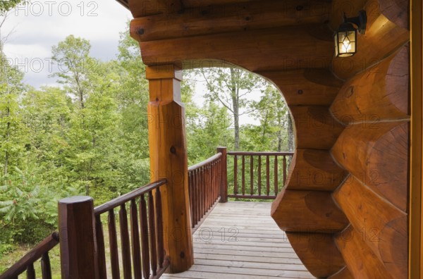 Brown reddish stained Scandinavian log cabin home with with arch and wall made of large chinked logs and grey wood plank veranda in summer, Quebec, Canada, North America