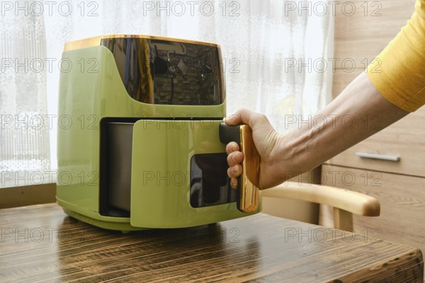 Modern air fryer in a bright kitchen with a person reaching to open the drawer