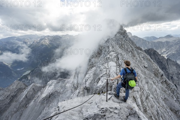 Mountaineer on a narrow rocky ridge on a steel cable, Watzmann crossing to Watzmann Mittelspitze, view of mountain panorama, Berchtesgaden National Park, Berchtesgaden Alps, Bavaria, Germany, Europe