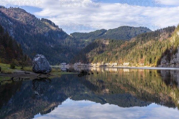 The Vordere Gosausee in autumn with a view of the Gasthof Gosausee. On the left a large rock on the lake shore, good weather, blue sky, clouds. Reflection. Top left the mountain station of the Gosaukammbahn cable car. Vorderer Gosausee, Gosau, Gosau valley, Salzkammergut, Upper Austria, Austria, Europe