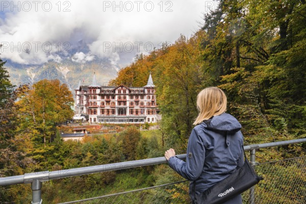 A woman looks from a railing at a large hotel surrounded by autumnal forest, Lake Brienz, Giessbach waterfall, Switzerland, Europe