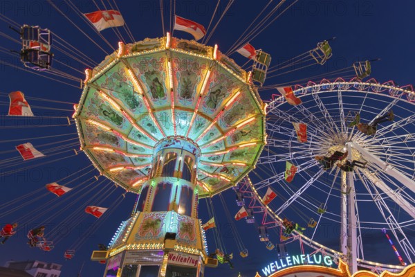 A funfair at dusk with illuminated chain carousel and Ferris wheel, Europa Rad, rides, wave flight, Cannstatter Wasen, folk festival, Bad Cannstatt, Stuttgart, Baden-Württemberg, Germany, Europe