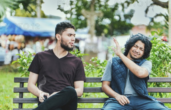 Man smoking and exhaling smoke to another person near him. Man smoking cigarette near people in public