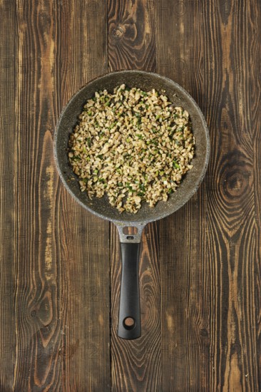 A skillet filled with sauteed diced mushrooms mixed with fresh herbs on a rustic wooden table. The dish showcases a blend of champignons and greens, ready for serving
