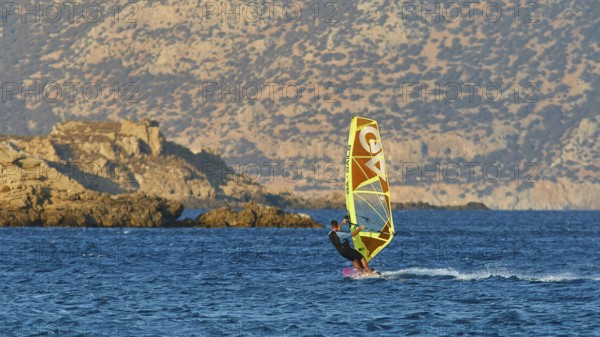 Person windsurfing in front of rocky coastal scenery and blue mountains in the background, windsurfer, Meltemi windsurfing spot, Devils Bay, Paralia Vatha, Vatha Beach, southeast coast, Karpathos, Dodecanese, Greek Islands, Greece, Europe