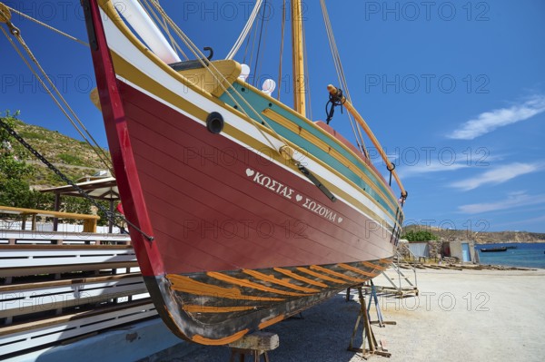 A colourful wooden boat hangs in a dry dock under a clear blue sky and calm atmosphere, Patmos Marine, boatyard, Diakofti, Patmos, Dodecanese, Greek Islands, Greece, Europe