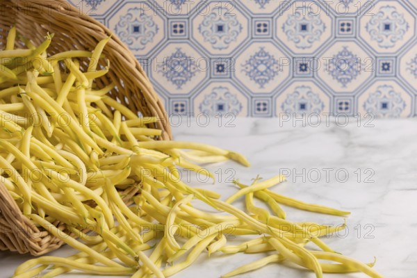 A basket of yellow beans tipped out on a marble worktop